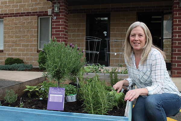 Cory Bowie, Event Coordinator and Waypoint Gardener, sitting next to the two garden pallets at 410 Woodland Ave in Bloomfield.